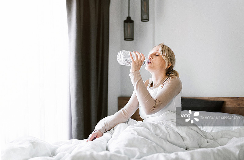 可爱的女人在舒适的床上醒来后喝水图片素材