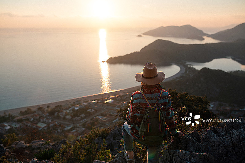 身穿时装、头戴帽子的女性在山顶观赏土耳其奥卢代尼兹海滩日落图片素材
