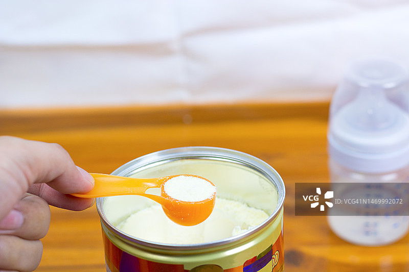 特写：浅色背景下的奶粉和蓝色勺子。罐中量勺里的婴儿奶粉，以及婴儿奶粉和奶瓶。图片素材