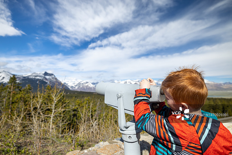 在加拿大艾伯塔省沃特顿国家公园用双筒望远镜观看景色的年轻红发男孩图片素材
