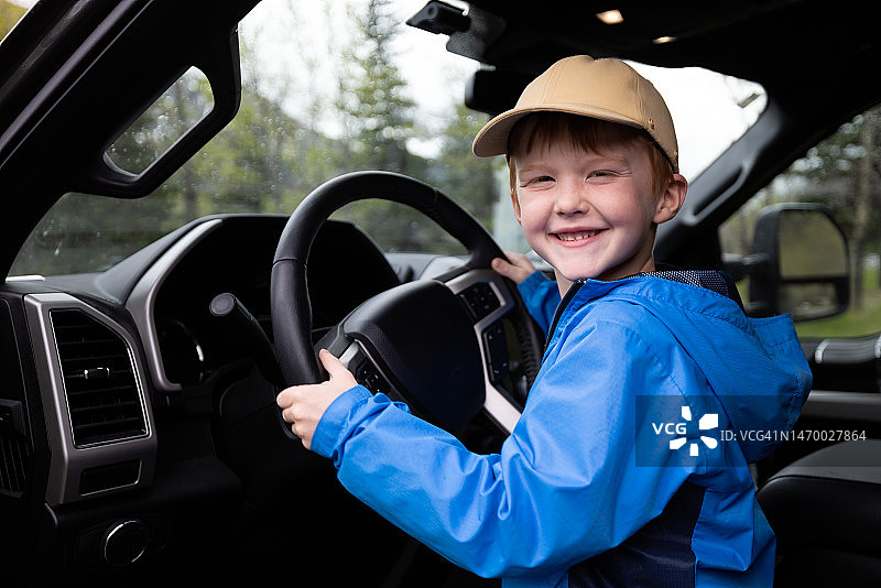 一个6岁的红发男孩在公路旅行中，坐在皮卡车里，对着镜头微笑图片素材