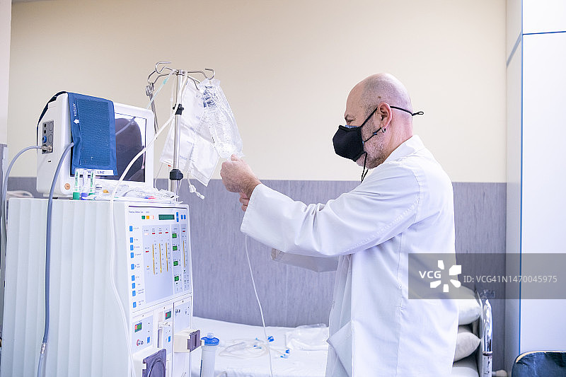 身穿白色工作服和防护面罩的技术员准备血液透析机图片素材
