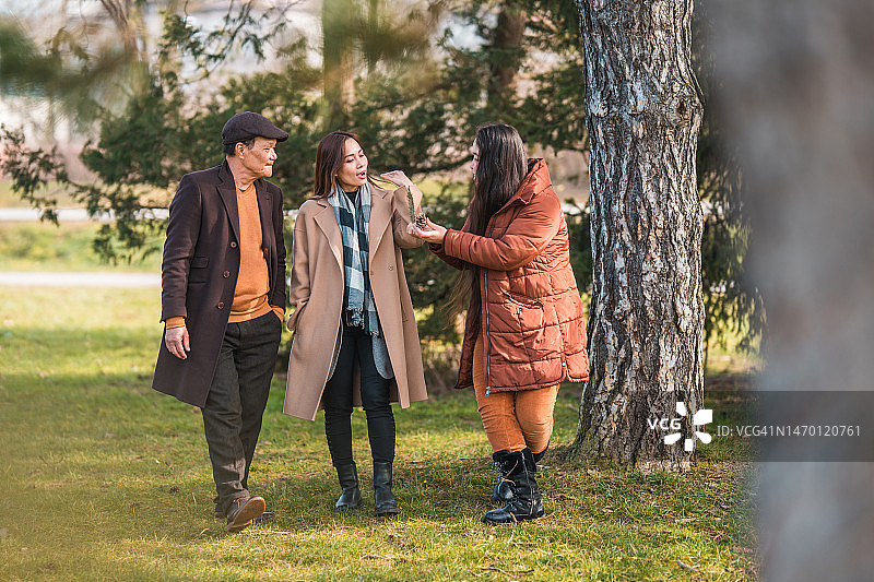 阳光明媚的冬日里在公园散步的亚洲家庭图片素材