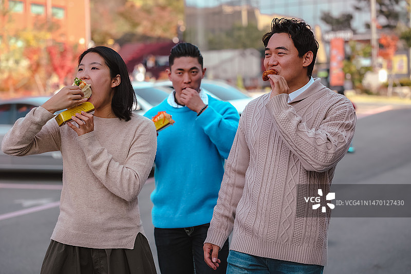 快乐的亚裔和欧洲朋友在首尔秋季的城市公园里散步、交谈和品尝纯素街头食品图片素材