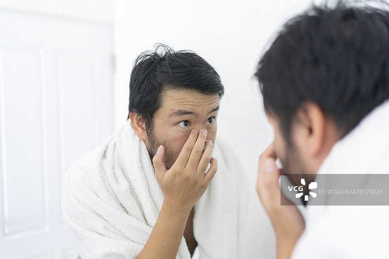 在浴室用镜子检查面部的亚洲成年男子图片素材