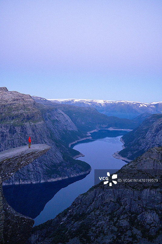 徒步男人站在挪威著名巨岩Trolltunga（巨魔之舌）上，俯瞰山谷全景图片素材