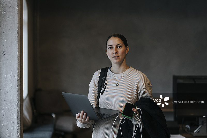 自信的女企业家在办公室手持笔记本电脑的肖像图片素材