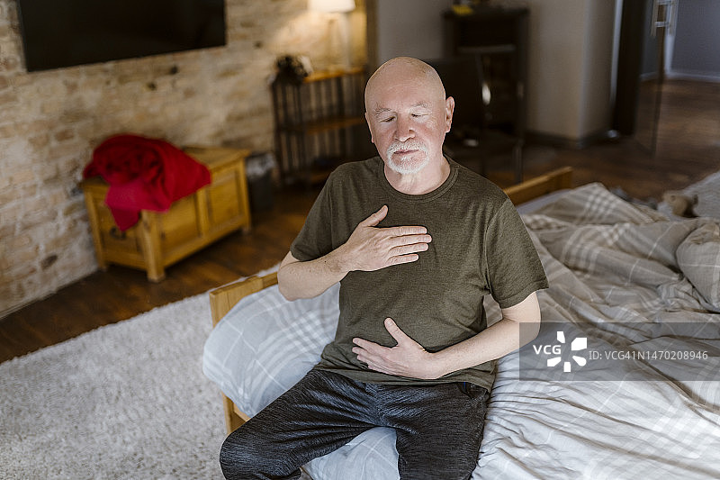 在家中床上闭着眼睛做呼吸运动的年长男子图片素材