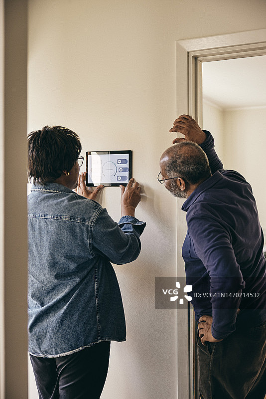 年长夫妇查看墙上的智能家居系统图片素材