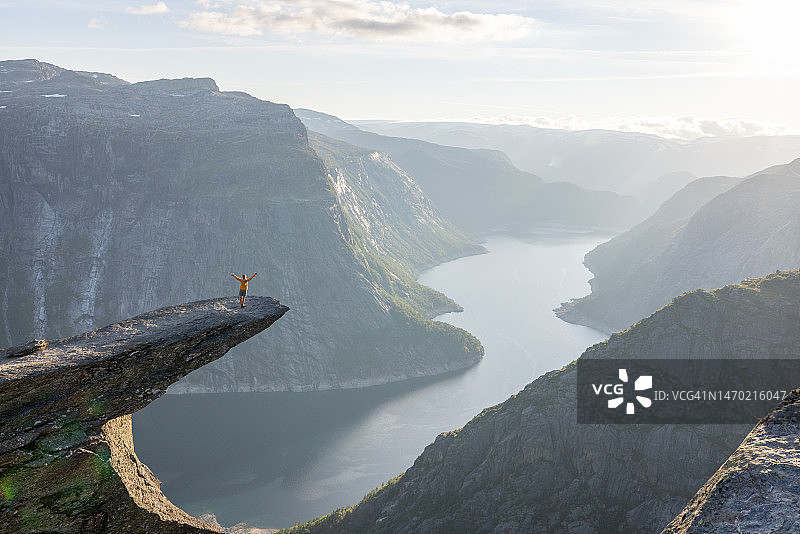 一位女士站在挪威罗加兰郡奥达附近,Trolltunga山悬崖边,Ringedalsvatnet湖上,张开双臂欣赏日落图片素材