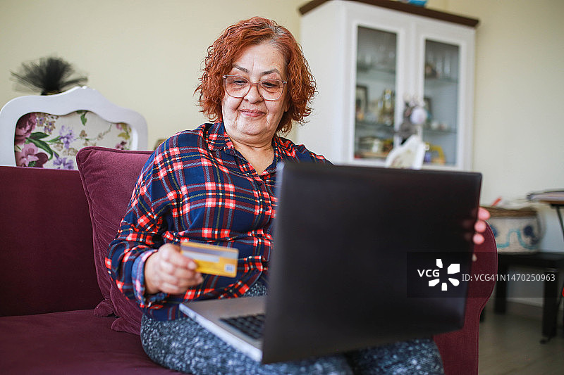 年长的女人在家里的客厅用笔记本电脑取消信用卡，怀疑有欺诈行为图片素材