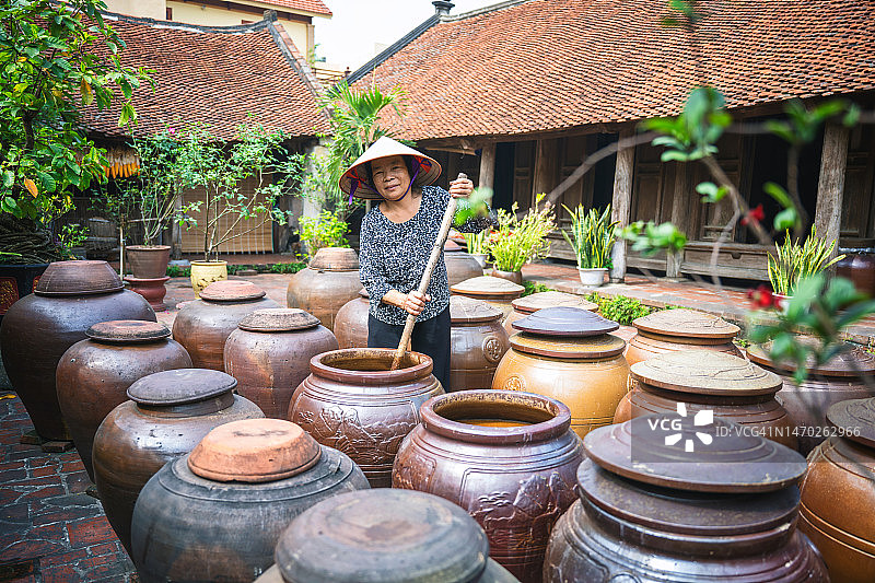 在庭院里搅拌巨大黏土大豆荚的越南老年妇女图片素材