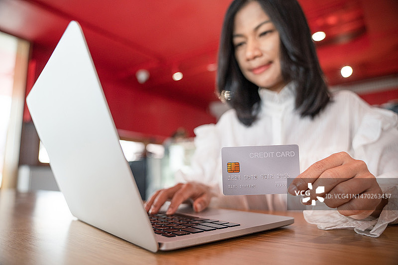 年轻女人手持信用卡使用笔记本电脑，用智能手机在线购物，在线销售，在线购物概念图片素材