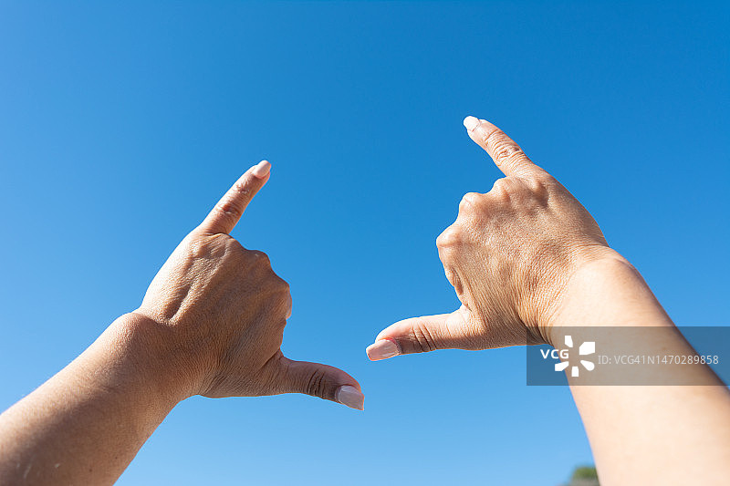 蓝色天空背景下，女人手势冲浪手势图片素材