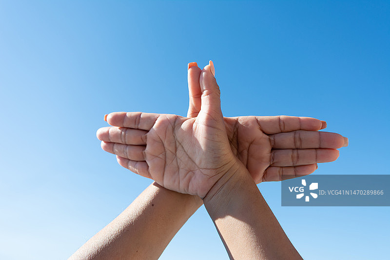 女人双手在蓝天下做出鸽子手势图片素材