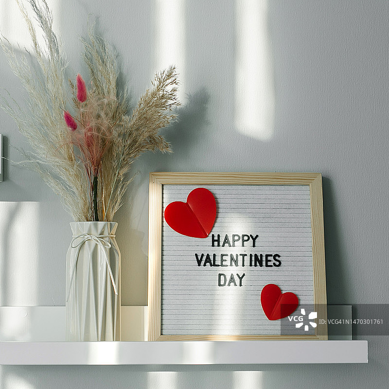 带有文字“情人节快乐”的字母板和花瓶，里面装着白色架子上的干花，位于哈萨克斯坦的房间里图片素材