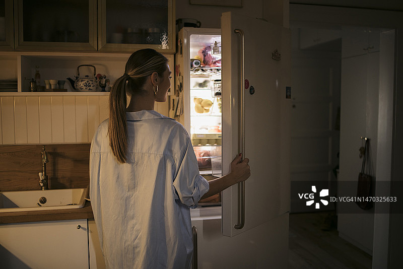 年轻女人深夜在冰箱里找食物，感到饥饿图片素材