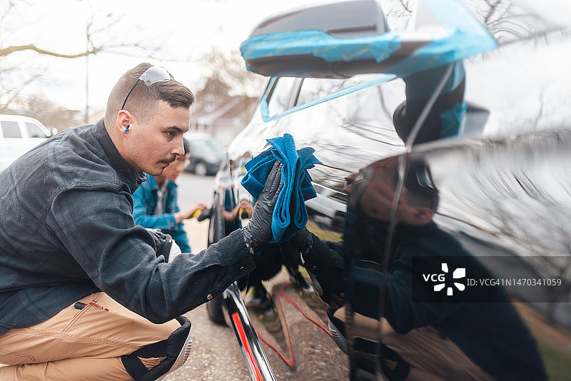 汽车细节：男人用超细纤维毛巾抛光黑色汽车，去除划痕，漆面修复，广角图片素材
