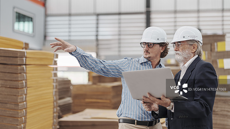 年长的商人在工厂里与经理一起查看笔记本电脑上的生产进度报告图片素材