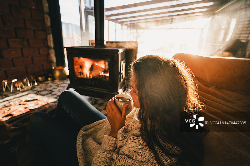 女人在壁炉前放松，抱着一杯热饮图片素材