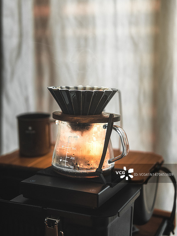 在桌子上进行手冲咖啡或滴滤咖啡。将水倒入咖啡滴滤器中冲泡咖啡，居家咖啡馆文化生活方式。图片素材