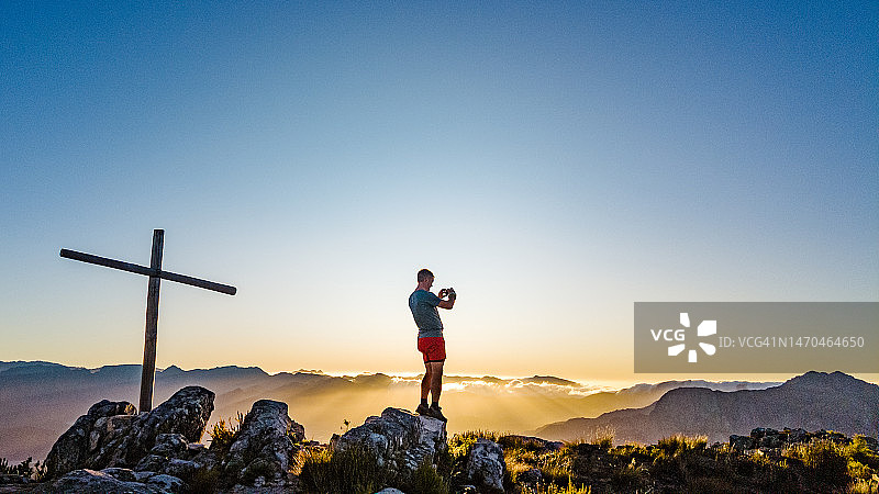 站在山顶十字架旁拍照的男子剪影图片素材