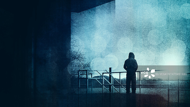 一个可怕的蒙面人向外看，背对着镜头。在阴森多雾的冬日里，以天空为背景，呈现出轮廓。经过了Grunge编辑。图片素材