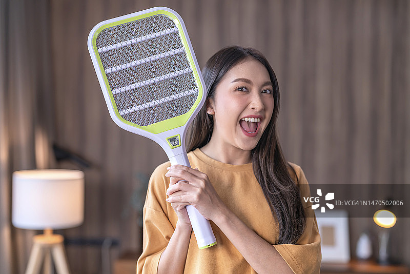 年轻的亚洲女性在家中使用电蚊拍驱赶蚊子图片素材
