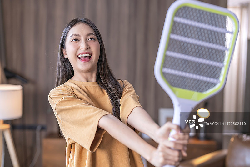 年轻的亚洲女性在家中使用电蚊拍驱赶蚊子图片素材