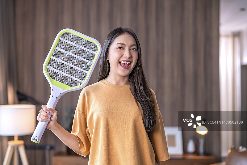 年轻的亚洲女性在家中使用电蚊拍驱赶蚊子图片素材