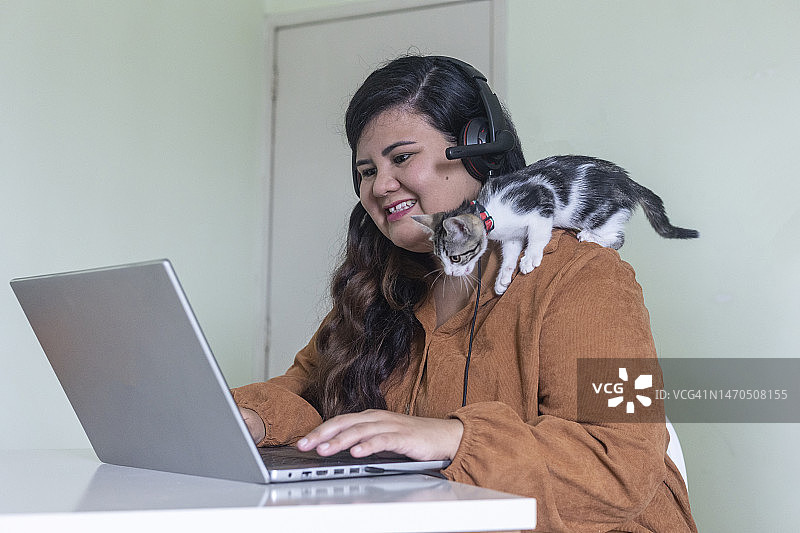 在家用笔记本电脑工作的拉丁裔女人和宠物猫图片素材