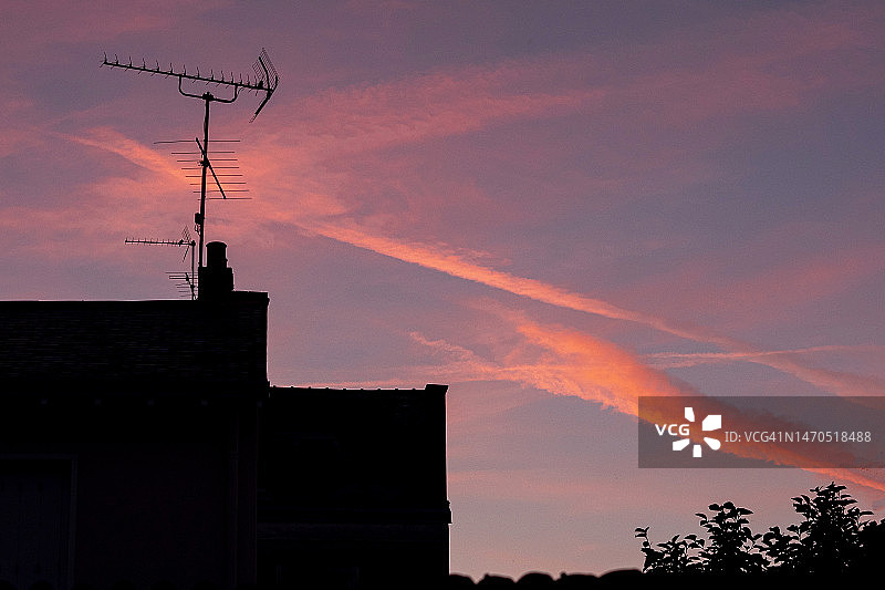日落时分建筑轮廓背景下的飞机尾迹图片素材