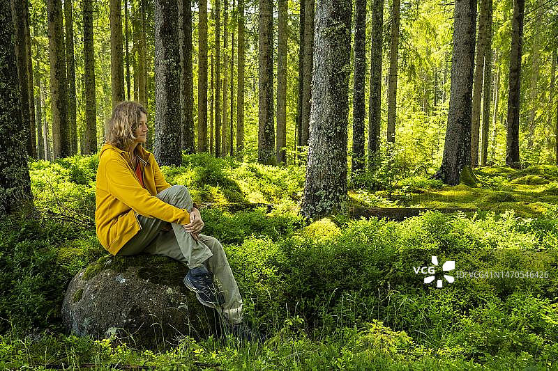 一位女士在德国巴登-符腾堡州黑森林中，放松地坐在大石头上享受自然图片素材
