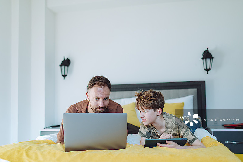父子在家使用笔记本电脑和平板电脑图片素材