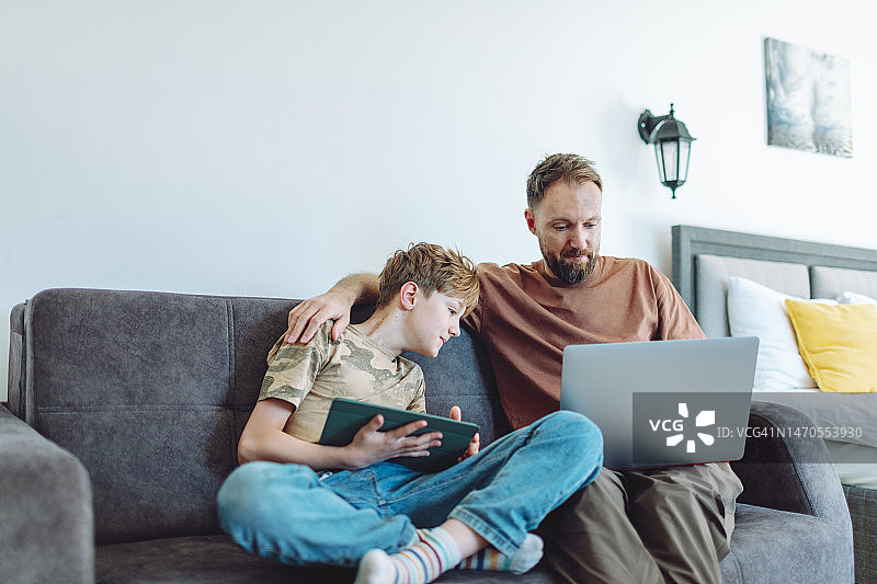 父子在家使用笔记本电脑和平板电脑图片素材