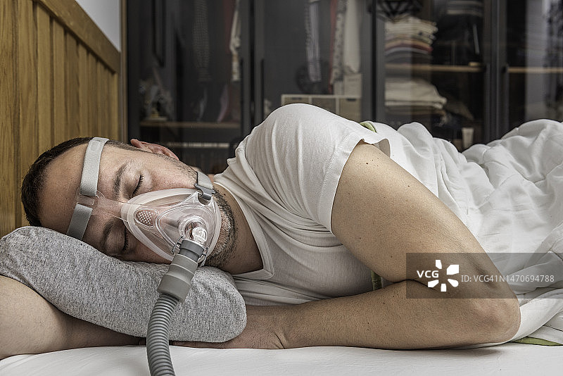 因阻塞性睡眠呼吸暂停而戴着CPAP面罩睡觉的男人图片素材