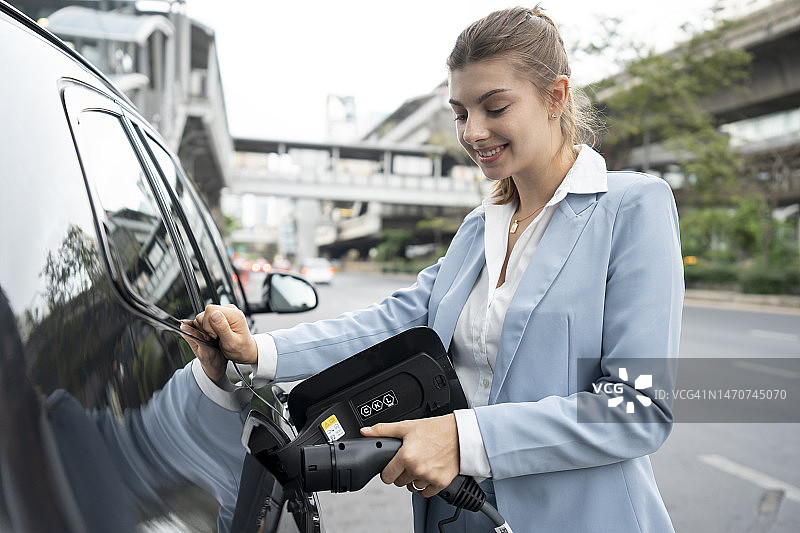 商务女人在城市里为她的电动汽车充电。图片素材