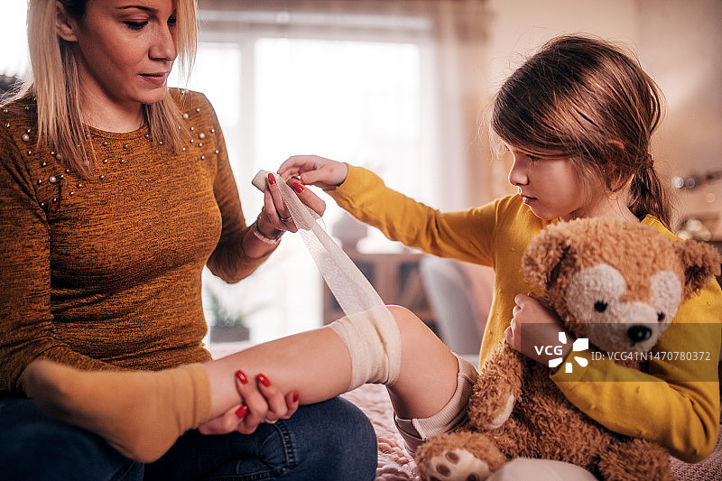 妈妈给女儿的腿包扎绷带，并一起玩泰迪熊图片素材