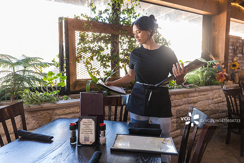 年轻女服务员在餐厅的空桌上放菜单图片素材