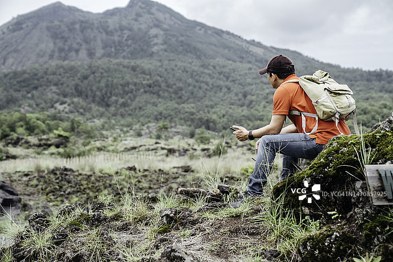 在巴厘岛巴图尔火山徒步旅行期间使用手机的亚洲男人图片素材