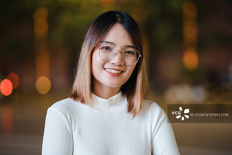 城市夜景中微笑看向镜头的年轻亚洲女性图片素材