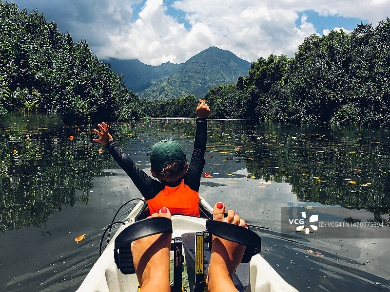 穿着莱卡防护服的男孩在河边与成人一起划皮划艇，山景图片素材