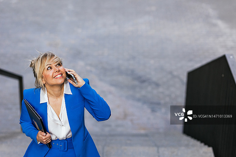 面带微笑，用笔记本电脑钦佩地看着城市摩天大楼的女商人图片素材