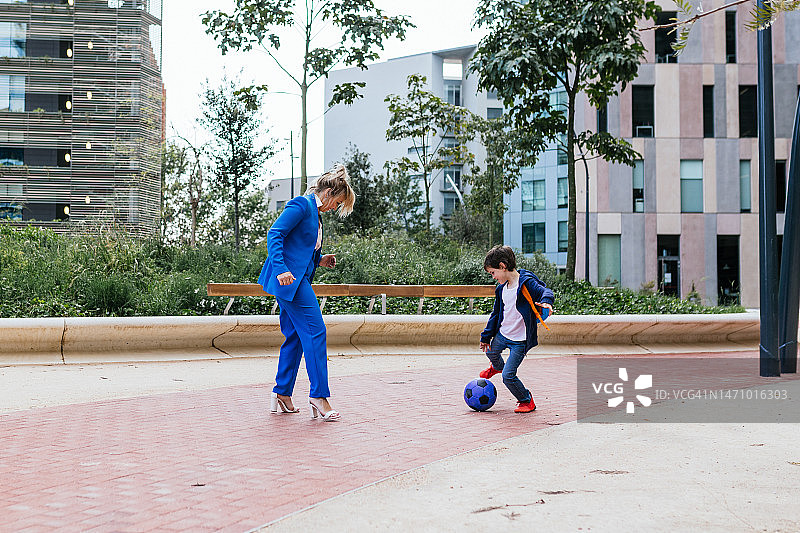 下班后穿着高跟鞋和儿子踢足球的女商人图片素材