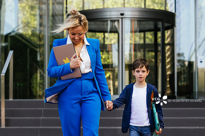 微笑的母亲穿着商务服装，牵着儿子的手下班图片素材