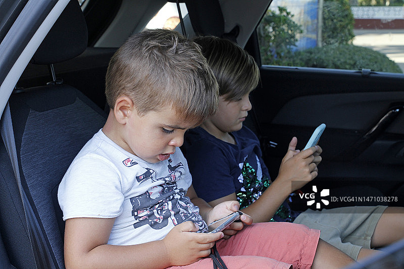 姐弟/兄妹在汽车座位上玩电子游戏图片素材