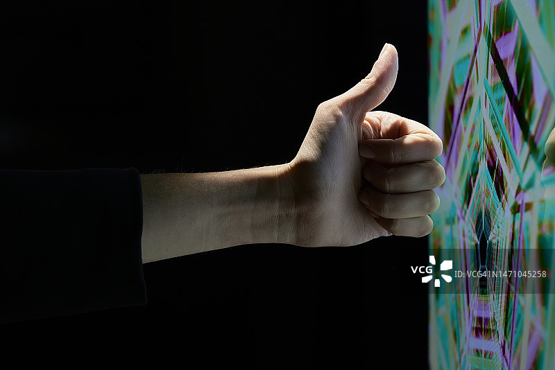 在彩色技术屏幕前，一个人的手竖起大拇指特写侧视图图片素材