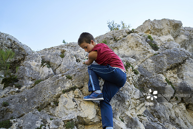 身穿运动服的男孩攀登岩石山丘，专注地向下看图片素材