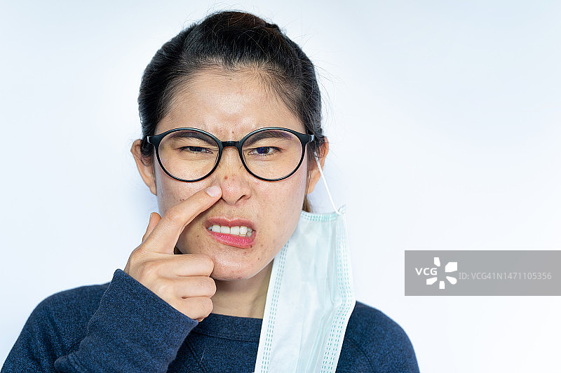 亚洲女人指着脸上因长时间佩戴口罩而出现的痤疮问题图片素材