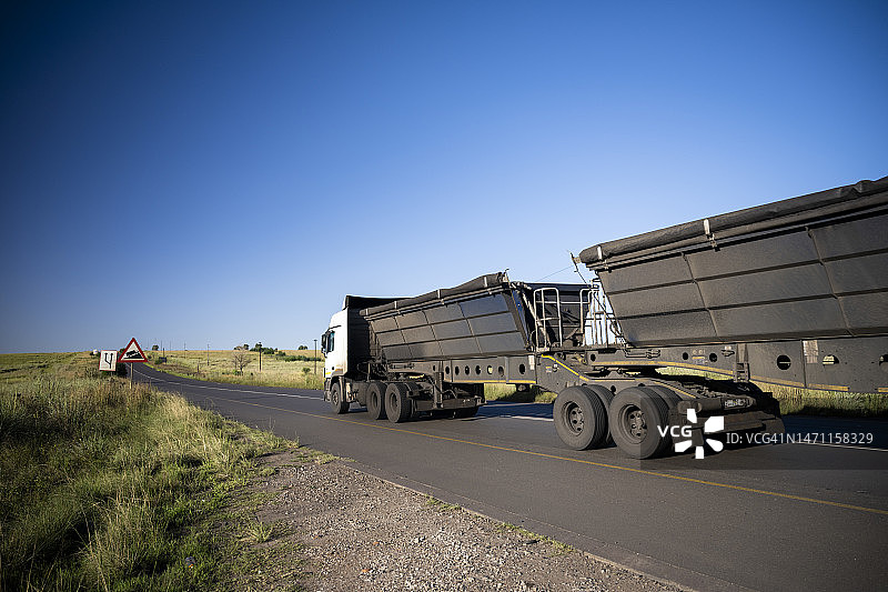行驶在道路上的黑色自卸卡车，晴朗的蓝天图片素材